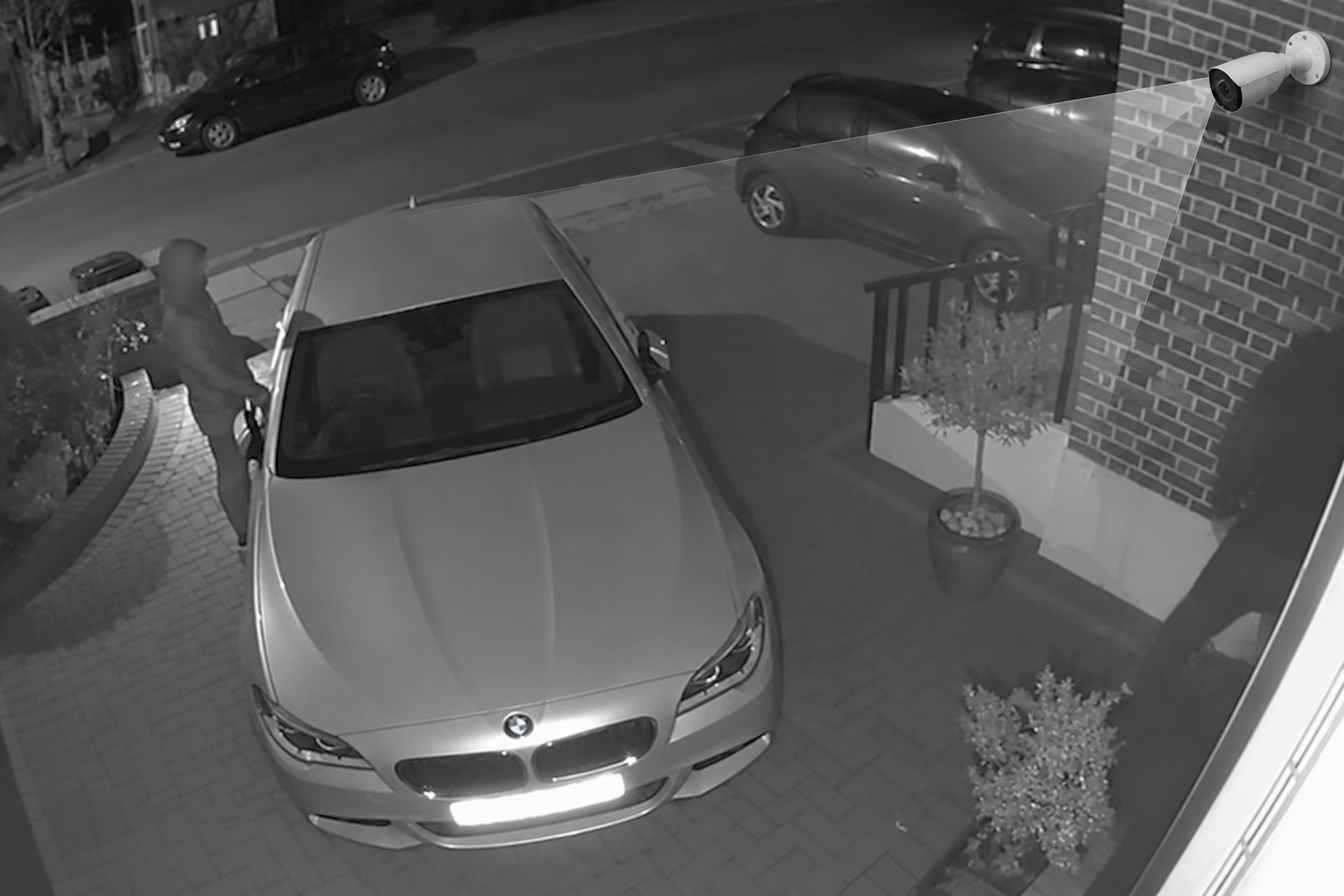 CCTV security camera mounted on a building, pointed at a car park and perimeter fence